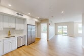 Unit 302 at 499 Atkinson Ave in Stoughton, MA is a thoughtfully designed one-bedroom, two-bathroom residence that blends modern finishes with functional living. Light hardwood flooring flows consistently throughout the unit, complementing the neutral, warm-toned walls that create a clean and inviting atmosphere.

The open-concept kitchen and living area forms the heart of the unit. The kitchen is outfitted with crisp white shaker cabinets, gold-accented hardware, a stainless steel sink with a gold faucet, and a full suite of stainless steel appliances including a refrigerator, range, microwave, and dishwasher. Recessed lighting brightens the space overhead. The adjacent living area is generously sized and filled with natural light from large windows and a sliding glass door that opens directly onto a private balcony with outdoor views of the surrounding greenery.

The spacious primary bedroom features a large window framing lush tree views, a flush-mount ceiling fixture, and ample room for furnishings. A hallway with built-in closet storage connects the rooms efficiently.

Both bathrooms are finished in a clean, contemporary style. The primary bath includes a walk-in shower, a white vanity with gold fixtures, and a large mirror. The layout is complemented by matte black door hardware that adds a modern contrast throughout the unit.
