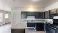 This single-story, 3-bedroom, 2-bathroom home offers a practical and comfortable layout designed for everyday living. The kitchen serves as a functional centerpiece, featuring dark espresso-toned shaker cabinets, speckled laminate countertops, a double-basin sink, and black appliances including a range, dishwasher, and refrigerator. A kitchen island provides additional prep space, while durable wood-look flooring runs throughout the kitchen and main living areas, adding warmth and easy maintenance.

The three bedrooms are finished with plush wall-to-wall carpet and neutral beige walls, creating a calm and inviting atmosphere. Each bedroom is equipped with a ceiling fan with light kit and features windows that allow natural light and outdoor views to filter in. The spacious primary bedroom includes two windows and offers a generous footprint. One of the secondary bedrooms includes a closet with built-in shelving.

The two bathrooms differ in configuration: one includes a full tub/shower combo with white surround and chrome fixtures, while the second is a more compact bathroom with wood-look flooring, a wall-mounted sink, and grab bar accessibility features. A hallway connects the main living areas to the bedrooms, completing this efficient and move-in-ready home.