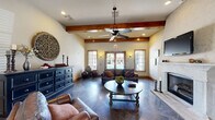 Located in Bixby, Oklahoma, this single-floor community space combines rustic charm with functional design across a thoughtfully arranged layout. The welcoming entrance greets visitors with soaring ceilings, a decorative tray ceiling detail, a pendant light fixture, and polished dark tile flooring that flows throughout the main areas. An elegant arched doorway leads from the entryway into the main gathering spaces.

The primary living room is a standout, featuring prominent exposed wood ceiling beams, a ceiling fan, a classic white fireplace with a raised hearth, and large wood-framed French doors and windows that invite abundant natural light and views of the outdoors. Rich leather seating, a round coffee table, and warm wall sconces contribute to the inviting ambiance.

A secondary living area, accessible through wood-framed French doors, provides additional recreational space complete with tile flooring and decorative wall art — currently set up with a foosball table, making it ideal for casual entertainment.

The kitchen is a striking focal point, anchored by a curved stone-clad breakfast bar with dark granite countertops, warm wood cabinetry, a custom range hood, and pendant lighting. Rich wood-toned flooring and a casual dining nook with seating complete this well-equipped space. A hallway connects the various areas seamlessly, reinforcing the cohesive and welcoming character of this community gathering space.