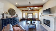 Located in Bixby, Oklahoma, this single-floor community space combines rustic charm with functional design across a thoughtfully arranged layout. The welcoming entrance greets visitors with soaring ceilings, a decorative tray ceiling detail, a pendant light fixture, and polished dark tile flooring that flows throughout the main areas. An elegant arched doorway leads from the entryway into the main gathering spaces.

The primary living room is a standout, featuring prominent exposed wood ceiling beams, a ceiling fan, a classic white fireplace with a raised hearth, and large wood-framed French doors and windows that invite abundant natural light and views of the outdoors. Rich leather seating, a round coffee table, and warm wall sconces contribute to the inviting ambiance.

A secondary living area, accessible through wood-framed French doors, provides additional recreational space complete with tile flooring and decorative wall art — currently set up with a foosball table, making it ideal for casual entertainment.

The kitchen is a striking focal point, anchored by a curved stone-clad breakfast bar with dark granite countertops, warm wood cabinetry, a custom range hood, and pendant lighting. Rich wood-toned flooring and a casual dining nook with seating complete this well-equipped space. A hallway connects the various areas seamlessly, reinforcing the cohesive and welcoming character of this community gathering space.