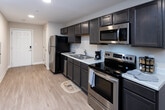 Located at 158 Bass Pro Dr in Sevierville, Tennessee, this single-floor unit offers a practical and well-appointed layout designed for comfortable living. The open-concept main area seamlessly connects the kitchen, dining, and living spaces, all unified by light-toned hardwood-style flooring that runs throughout.

The kitchen is a standout feature, outfitted with dark gray shaker-style cabinetry extending to the upper walls, light countertops, and a full suite of stainless steel appliances including a refrigerator, electric range, over-the-range microwave, and dishwasher. Recessed lighting illuminates the space efficiently. The kitchen flows directly into the dining area and a cozy living room, where a window at the far end brings in natural light.

The bedroom provides a calm retreat with neutral wall tones, a window with blinds, and a closet with bifold doors offering built-in storage. The bathroom features a walk-in shower with a curtain enclosure, hardwood-style flooring, and a clean, minimalist design with warm beige walls. The overall ambiance throughout the unit is understated and functional, with a neutral color palette creating a cohesive, move-in-ready feel.