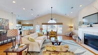 Located at 346 Shadow Creek Ln in Anderson, South Carolina, this single-floor space offers a thoughtfully designed open-plan layout that seamlessly connects the living and dining areas. The most striking architectural feature is the soaring vaulted ceiling, which amplifies the sense of openness and volume throughout the main living area. A ceiling fan is centrally mounted, adding both function and visual interest beneath the high roofline.

Warm hardwood floors run throughout the space, providing a cohesive foundation that complements the neutral, cream-toned walls. Large windows adorned with decorative valances flood the interior with natural light and offer views of the surrounding neighborhood. An arched transom window adds a refined architectural touch near the entryway.

The living area is anchored by a classic white-tiled fireplace with a mantel, which serves as a natural focal point. Multiple seating arrangements allow for versatile use of the space. The adjacent dining area features direct access to the outdoors through a glass-paneled door, further enhancing the connection between interior and exterior.

A kitchen with bar-height seating and standard appliances is visible from the dining zone, reinforcing the open and interconnected nature of the floor plan. Recessed lighting complements the natural light throughout. Overall, the space presents a warm, welcoming ambiance with clean lines and bright, airy interiors.