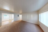 Located in Seattle's Seward Park neighborhood, this single-story, 3-bedroom, 1-bathroom home offers a practical and well-organized layout. The living room is a spacious, open area finished with warm neutral carpet and crisp white walls, allowing natural light to filter in through the windows and creating a bright, welcoming atmosphere. A central hallway connects the living spaces to the three bedrooms, each of which features soft carpeting, white walls, and windows with vertical blinds that bring in natural light. Baseboard heating is present in the bedrooms, ensuring comfort throughout the seasons. The primary bedroom offers a generous footprint with dedicated closet space. The kitchen is equipped with warm-toned wood cabinetry, a black appliance suite including a range, microwave, and refrigerator, and light hardwood-style flooring that adds a clean, modern touch. The full bathroom includes a wood-vanity with a marble-style countertop, a mirrored medicine cabinet, and brushed nickel fixtures. An in-unit laundry area adds convenience. With four closets throughout, storage is plentiful. The home's clean, neutral palette provides a versatile canvas throughout.