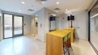 Located on S Charles St in Baltimore's 21230 corridor, this single-floor commercial space delivers a contemporary, design-forward environment suited for collaborative work and professional gatherings. The layout combines open-plan work areas with enclosed meeting rooms, offering flexibility for a variety of uses.

The main open area features light wood high-top tables paired with green upholstered bar stools, illuminated by bold cylindrical pendant lamps and recessed ceiling lights. Light-toned flooring and soft grey walls maintain a clean, neutral backdrop throughout. A courtyard-access door provides connectivity to an exterior area, adding a practical element to the layout.

Glass-partitioned meeting rooms lend the space a sense of transparency and openness without sacrificing privacy. One enclosed room features textured dark wallcovering, a round table, and modern upholstered chairs, while another showcases a striking geometric mural in teal, black, and white with linear LED lighting overhead, creating a visually dynamic atmosphere. A colorful typographic artwork is prominently displayed near the glass enclosure, adding an artistic focal point.

Additional areas include an open, carpeted room with floor-to-ceiling glazing that invites natural light. Throughout, polished concrete and light flooring, crisp white ceilings, and curated artwork contribute to a cohesive, professional ambiance with distinct creative energy.