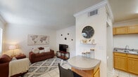 This single-story space offers a functional and cohesive layout connecting the living area, kitchen, bedroom, and bathroom. The living room is finished with light ceramic tile flooring, white crown molding, and neutral walls, creating a bright and clean atmosphere. A peninsula counter with seating separates the living area from the kitchen, providing a convenient breakfast bar and defining each space without sacrificing openness. The kitchen features warm oak cabinetry, granite-toned countertops, stainless steel appliances including a full-size refrigerator, a double sink, and continued tile flooring, offering ample storage and a practical workspace.

The bedroom is a comfortable retreat with dark hardwood-style flooring, a ceiling fan, and a window dressed with sheer curtains that allows natural light to filter in. The room provides enough space for a bed and a dedicated desk area. The bathroom is efficiently designed with a wood-toned vanity, a granite-style countertop, a large mirror, and a shower-tub combination, all finished in light tile. Throughout the space, crown molding and consistent neutral tones contribute to a cohesive and well-maintained interior.