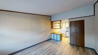 Located at 1056 Mindy Ln in Wooster, Ohio, this single-floor unit offers a thoughtfully arranged layout comprising a living room, kitchen, and bathroom. Light gray luxury vinyl plank flooring runs throughout, lending a clean, cohesive look to the entire space.

The living area greets visitors at the entry, where a dark wood-paneled door opens to a bright room with a large window that allows natural light in while offering a view of the surrounding neighborhood. A wall-mounted PTAC heating and cooling unit ensures year-round comfort. Crown molding with warm wood-toned trim accents the walls and ceiling throughout the unit, adding a subtle decorative detail.

The kitchen is efficiently designed with an open peninsula featuring a laminate countertop and retro-style light blue cabinetry below, providing convenient storage. Open shelving above the peninsula connects visually to the galley-style kitchen beyond, which is equipped with a white electric range, white cabinetry, and a single-basin sink. A textured popcorn ceiling adds character to the kitchen area.

The bathroom is clean and functional, featuring a single-sink vanity with a granite-style countertop, a framed mirror, a tub-shower combination, and light gray walls. Chrome towel bars and a toilet complete the space. A closet with wooden sliding doors provides additional storage near the living area.