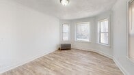 Located at 7609 S Coles Ave in Chicago's South Side, this well-appointed 1-bedroom, 1-bathroom unit offers a clean, bright, and efficiently designed living space spread across a single floor. Light-toned hardwood flooring runs throughout, complementing the crisp white walls and trim that give the home a fresh, airy feel. The living room is a standout feature, boasting a curved bay window arrangement that allows generous natural light to fill the room, alongside a classic cast-iron radiator that adds vintage Chicago character. The bedroom is a comfortable size, with multiple windows providing additional natural light and ventilation, plus its own radiator for warmth. The kitchen is thoughtfully updated with gray shaker-style cabinetry, marble-look countertops, a stainless steel sink, and a full-size refrigerator, with a pantry nearby for added storage convenience. Two closets throughout the unit provide practical storage solutions. The bathroom features a clean, fully tiled shower-tub combo with chrome fixtures. A connecting hallway ties the layout together smoothly. With its textured ceilings, updated finishes, and classic architectural touches, this unit offers a cozy and functional home in a well-established Chicago neighborhood.