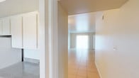 This single-story space is designed with a clean, functional layout that flows naturally from room to room. The main living area is generously sized, featuring light-toned tile flooring and neutral cream walls that enhance the brightness brought in by large vertical-blind-covered sliding doors and windows. A ceiling fan with a light fixture adds a practical finishing touch overhead.

The galley-style kitchen runs along one wall, outfitted with white cabinetry offering ample storage, a coil-burner electric range, a double-basin sink with speckled countertops, and a full-size refrigerator. Dark wood-look vinyl flooring runs throughout the kitchen, providing a warm contrast to the white cabinetry.

The bedroom is carpeted and features its own ceiling fan, a window for natural light, and a large sliding glass door fitted with vertical blinds, allowing direct access to the outdoors and filling the room with additional natural light.

The bathroom is clean and straightforward, with white cabinetry, a speckled countertop vanity, a tub-shower combination, and wood-look vinyl flooring that coordinates with the kitchen. Overall, the space presents a bright, neutral palette throughout.