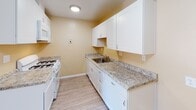 This single-floor unit offers a clean, functional layout designed for comfortable everyday living. Throughout the space, light wood-style flooring and warm golden-beige walls create a cohesive and inviting atmosphere, complemented by white trim and textured ceilings.

The open living area is generously sized, featuring a wall-mounted air conditioning unit and a sliding glass door that fills the room with natural light and provides access to an outdoor space. The layout connects seamlessly to the kitchen, which is well-appointed with crisp white shaker-style cabinetry, granite-style countertops, a stainless steel sink, and white gas appliances including a range and over-the-range microwave — all beneath a bright flush-mount light fixture.

A hallway with a skylight-style ceiling fixture leads to the private areas of the unit. The bedroom is a comfortable, well-lit room with a window dressed in blinds and a reach-in closet featuring built-in shelving and hanging rods for ample storage.

The full bathroom is finished with warm yellow walls, a tiled combination tub and shower with a curved curtain rod, a white vanity, and classic mosaic tile flooring — providing a clean and practical space. Overall, the unit presents a move-in-ready interior with a bright, neutral palette throughout.