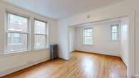 This single-floor residence showcases classic architectural details throughout its well-organized layout. Warm, honey-toned hardwood floors run continuously through the living areas and bedrooms, lending a sense of cohesion and timeless character to the space. Crown molding accents the ceilings, adding a refined touch to the otherwise clean, white-painted walls.

The living and dining areas flow openly into one another through a wide arched passageway, creating a generous, connected feel. Multiple double-hung windows frame views of surrounding greenery and neighboring architecture, filling the rooms with ample natural light. Cast-iron radiators positioned throughout provide classic, efficient heating and serve as charming period details.

The kitchen is efficiently designed with warm wood cabinetry, granite countertops, a subway tile backsplash, a stainless steel sink, and light ceramic tile flooring. A window above the sink brings in natural light. Built-in open shelving adds practical storage within the kitchen space.

The bathroom features a full-size soaking tub with an overhead shower, a window for natural ventilation, a vanity, and built-in wall shelving for added storage.

Additional rooms offer versatile spaces suitable for bedrooms or a home office, each with hardwood floors, white walls, and natural light. A dedicated closet and entry area complete the functional layout of this classically detailed residence.