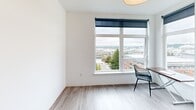Located on the eighth floor of 1552 Market Street in downtown Tacoma, Washington, unit 805 is a thoughtfully designed studio offering an efficient, single-level layout. The space features light wood-look flooring throughout, crisp white walls, and recessed lighting that contribute to a clean, modern aesthetic.

The kitchen is a standout feature, lined with white flat-front cabinetry extending from floor to ceiling, offering generous storage. A stainless steel refrigerator, built-in microwave, and undermount sink complete the functional setup, while open shelving adds a stylish display area. The kitchen flows seamlessly into the main living area, maximizing the sense of openness.

The living area benefits from a large picture window fitted with a roller shade, framing elevated views of the Tacoma cityscape and surrounding neighborhoods. Natural light fills the space throughout the day, enhancing the bright, airy atmosphere. A dedicated nook provides space for a desk and chair, making it suitable for remote work.

The bathroom includes a tub-shower combination with white tile surround, wood-look tile flooring, and clean white fixtures, maintaining the consistent modern palette found throughout the unit.

Overall, unit 805 offers a well-organized, light-filled living environment with contemporary finishes and commanding urban views in the heart of downtown Tacoma.