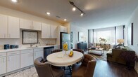Located at 11001 W 15th Pl in Lakewood, Colorado, this single-floor residence offers a thoughtfully designed open-concept layout that seamlessly connects the kitchen, dining, and living areas. The kitchen is equipped with stainless steel appliances — including a refrigerator, dishwasher, microwave, and range — complemented by white cabinetry with sleek hardware and light countertops. Wood-look flooring runs throughout the main living areas, adding warmth and continuity. The dining area accommodates a round table with upholstered chairs, positioned directly adjacent to the kitchen for convenient everyday use. The living room is bathed in natural light from large windows with blinds and draping curtains, creating a bright and welcoming atmosphere. The bedroom features plush carpeting, generous windows, and ample space for a full bedroom suite. Two bathrooms serve the residence: one with a vanity and wood-look flooring, and a second en-suite bathroom with a glass-enclosed shower, dual vanity, and direct access to the bedroom. Recessed and track lighting throughout provide effective illumination. The overall design is neutral and modern, offering a clean, comfortable living environment in the heart of Lakewood.