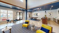 Located at 3830 NC-55 E in Durham, NC, this single-floor clubhouse for Elevate the Park is a thoughtfully designed community space that blends modern aesthetics with functional amenities. The interior is defined by soaring vaulted ceilings, bold navy and steel-blue accent walls, warm wood beam detailing, and polished concrete floors that lend an open, airy feel throughout.

The expansive living and lounge area serves as the heart of the space, anchored by a double-sided fireplace framed in warm wood, a wall-mounted TV, and a built-in bench seating nook. Vibrant yellow and navy accent furnishings — including plush sofas and lounge chairs — create inviting gathering zones. A billiards table adds a recreational focal point, while sculptural star-shaped acoustic ceiling panels double as striking design elements.

The kitchenette features a marble-look tile backsplash, a wooden island with bar seating, pendant lighting in coordinating blue tones, and a coffee station — ideal for casual entertaining. Adjacent dining seating and large windows offer abundant natural light and outdoor views.

Two private offices provide focused work environments: one features a sliding barn door, natural light, and curated artwork, while the second offers an intimate, tiled accent wall and dedicated task lighting — both designed for productivity and privacy.