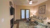 Located at 5201 Lakeland Blvd in Flowood, Mississippi, this single-floor residence offers a well-appointed and comfortable living environment. The living area serves as the heart of the home, showcasing warm neutral-toned walls that create an inviting and relaxed atmosphere. A standout feature is the fireplace with a tiled surround, adding both character and coziness to the space. Rich hardwood-style flooring runs throughout, complemented by a plush area rug that defines the seating area. A ceiling fan with a light fixture ensures year-round comfort, while a wall-mounted flat-screen television adds a modern touch. French doors with blinds open to the outdoors, allowing natural light to filter into the room and providing convenient access to the exterior. The living space is thoughtfully arranged with a neutral-toned sofa, a wooden coffee table, and coordinating accent pieces that contribute to the home's warm, welcoming character. The overall design reflects a practical yet stylish aesthetic, with attention to detail in the finishes and fixtures that make this Flowood residence a comfortable and functional place to call home.