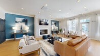 Located at Coventry Commons in Concord, NC, this thoughtfully designed single-floor space offers a versatile and welcoming environment across two living areas and a well-appointed kitchen. Wide-plank hardwood flooring flows seamlessly throughout, anchoring each room with warmth and continuity.

The main living area is a standout, featuring a tile-surround fireplace flanked by bold teal accent walls and curated artwork. Recessed lighting illuminates a comfortable mix of leather and upholstered seating, while a wall-mounted TV and an adjacent dining nook with large windows bring both function and natural light to the space. A sliding barn door connects to the secondary living area, which offers a more intimate setting with a shiplap-paneled feature wall, built-in shelving, a wet bar with marble countertops, and a wall-mounted TV — ideal for casual gatherings or media use. A third flexible area, accented by a striking geometric-patterned wallcovering, provides dedicated workspace with desks and lounge seating bathed in natural light from oversized windows.

The kitchen is outfitted with crisp white cabinetry, granite countertops, a vibrant blue tile backsplash, and stainless steel appliances, including a French door refrigerator. Crown molding and recessed lighting lend a polished finish to this highly functional and visually cohesive space.