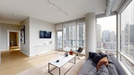 Located on W Huron Street in Chicago's vibrant River North neighborhood, this single-floor unit showcases a sleek, modern design with an open, airy layout. Light hardwood flooring runs throughout, complementing the neutral palette of soft grays and whites that define the interior aesthetic.

The living area is a standout space, anchored by expansive floor-to-ceiling windows that wrap around the room, flooding it with natural light and framing breathtaking panoramic views of the Chicago skyline. Track lighting overhead and a wall-mounted television add functional style, while a private balcony access door extends the living experience outdoors.

The kitchen is well-appointed with flat-front gray cabinetry, white tile backsplash, stainless steel appliances including a gas range and refrigerator, and a central island that doubles as a casual dining surface. An adjacent dining area provides additional space for gathering.

The bedroom continues the modern aesthetic with large windows offering city views, hardwood floors, and generous proportions. A clean, light-filled hallway with built-in storage connects the rooms seamlessly.

The bathroom features marble-look tile flooring, full marble-tiled surround at the soaking tub, and a streamlined vanity, creating a spa-like atmosphere.