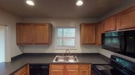 Located at 714 Connors Dr in Greenwood, Indiana, this single-floor residence offers a practical and well-organized layout. The kitchen is equipped with warm-toned wood cabinetry, dark speckled countertops, a double stainless steel sink, and black appliances including a dishwasher, electric range, and microwave. A window above the sink allows natural light to brighten the workspace. The living area is generously sized, featuring neutral carpet flooring, a textured ceiling, and a sliding glass door that opens to an outdoor view, alongside a secondary window that further enhances natural light. The bedrooms are carpeted and well-proportioned, each featuring windows that bring in outdoor light and views of the surrounding area. Closet storage is provided in the bedrooms, with one room offering a sliding-door closet and direct access to a bathroom. The bathroom includes a wood-toned vanity with dark countertop, a large mirror with overhead lighting, a tub-shower combination with tile surround, and hardwood-style flooring. Throughout the residence, the design is clean and functional, with a consistent neutral palette that provides a versatile backdrop for a variety of interior styles.
