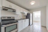 Located at 396 Queens Ave in London, Ontario, this 2-bedroom, 2-bathroom unit offers a clean, modern interior across a single, well-organized floor. The space is finished with light wood-style flooring throughout the main living areas, complemented by crisp white walls that create a bright and airy atmosphere.

The living room is generously proportioned, featuring large windows that frame views of the surrounding London cityscape, allowing abundant natural light to fill the space. The kitchen is thoughtfully designed with white shaker-style cabinetry, grey countertops, a subway tile backsplash, a stainless steel sink with a modern faucet, and an electric range with a built-in range hood.

The primary bedroom is a comfortable size, equipped with direct access to one of the two bathrooms and an additional closet, providing practical convenience. The second bedroom also benefits from natural light and urban views through its windows. Both bathrooms are finished in neutral tones with tile flooring; one includes a full bathtub and vanity.

A central hallway connects the rooms efficiently, and the overall layout makes excellent use of the available space. The consistent use of white finishes and light flooring throughout gives the unit a cohesive, contemporary feel suited to urban living in downtown London.