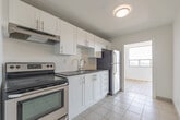 Located at 396 Queens Ave in London, Ontario, this 2-bedroom, 2-bathroom unit offers a clean, modern interior across a single, well-organized floor. The space is finished with light wood-style flooring throughout the main living areas, complemented by crisp white walls that create a bright and airy atmosphere.

The living room is generously proportioned, featuring large windows that frame views of the surrounding London cityscape, allowing abundant natural light to fill the space. The kitchen is thoughtfully designed with white shaker-style cabinetry, grey countertops, a subway tile backsplash, a stainless steel sink with a modern faucet, and an electric range with a built-in range hood.

The primary bedroom is a comfortable size, equipped with direct access to one of the two bathrooms and an additional closet, providing practical convenience. The second bedroom also benefits from natural light and urban views through its windows. Both bathrooms are finished in neutral tones with tile flooring; one includes a full bathtub and vanity.

A central hallway connects the rooms efficiently, and the overall layout makes excellent use of the available space. The consistent use of white finishes and light flooring throughout gives the unit a cohesive, contemporary feel suited to urban living in downtown London.