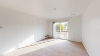 This single-floor unit offers a clean, functional layout with a bright and neutral aesthetic throughout. The main living area is generously sized, finished with plush wall-to-wall carpeting and crisp white walls that reflect natural light. A sliding glass door opens directly onto a private balcony equipped with a wooden railing, providing pleasant outdoor views of surrounding greenery and neighboring structures. The room is served by floor-level heating vents, ensuring year-round comfort.

The bedrooms continue the carpeted flooring and white-wall palette. One bedroom features a large window with vertical blinds, while another benefits from a walk-in closet with dual shelving on both sides, offering ample storage capacity.

The galley-style kitchen is efficiently arranged with upper and lower cabinetry in a warm oak finish, light-toned laminate countertops, and wood-look flooring. White appliances, including an electric range and refrigerator, are included. A dedicated laundry area with in-unit washer and dryer hookups provides added convenience.

The bathroom features an oak vanity with a wide laminate countertop, an integrated sink, a large wall mirror, and wood-look flooring, creating a practical and tidy space. Overall, the unit presents a straightforward, well-maintained environment with ample natural light.
