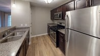 This single-story unit offers a well-designed layout with a neutral gray color palette and clean white trim throughout. The living area features warm wood-style flooring, a ceiling fan, and a sliding glass door with windows that invite natural light. Vaulted ceilings in the adjoining dining space add an open, airy feel, complemented by a chandelier overhead.

The kitchen is equipped with dark espresso cabinetry, granite countertops, and a full suite of stainless steel appliances including a gas range, built-in microwave, and refrigerator. A breakfast bar provides additional seating and connects the kitchen to the main living area, while a pendant light adds a finishing touch.

The bedrooms are carpeted for comfort, with generous proportions and access to walk-in closets. The primary bathroom features dark cabinetry with a granite-topped vanity, a large mirror with overhead lighting, and wood-style flooring. A walk-in closet is accessible directly from the bathroom, adding practical convenience.

Overall, the unit presents a consistent, modern aesthetic with thoughtful finishes throughout.