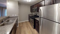 This single-story unit offers a well-designed layout with a neutral gray color palette and clean white trim throughout. The living area features warm wood-style flooring, a ceiling fan, and a sliding glass door with windows that invite natural light. Vaulted ceilings in the adjoining dining space add an open, airy feel, complemented by a chandelier overhead.

The kitchen is equipped with dark espresso cabinetry, granite countertops, and a full suite of stainless steel appliances including a gas range, built-in microwave, and refrigerator. A breakfast bar provides additional seating and connects the kitchen to the main living area, while a pendant light adds a finishing touch.

The bedrooms are carpeted for comfort, with generous proportions and access to walk-in closets. The primary bathroom features dark cabinetry with a granite-topped vanity, a large mirror with overhead lighting, and wood-style flooring. A walk-in closet is accessible directly from the bathroom, adding practical convenience.

Overall, the unit presents a consistent, modern aesthetic with thoughtful finishes throughout.