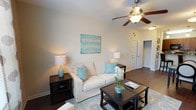 Located at 1001 Hayes Ln in Holly Springs, NC, this single-floor residence offers a thoughtfully designed layout with a cohesive, neutral color palette accented by soft blue tones throughout. The living room features rich hardwood-style flooring, a ceiling fan with light fixture, and natural light from front-facing windows, creating a warm and inviting atmosphere. The kitchen is equipped with rich cherry wood cabinetry, dark granite countertops, a tile backsplash, black appliances, and a peninsula breakfast bar with pendant lighting — ideal for casual dining or entertaining. Adjacent to the kitchen, the dining area showcases the same hardwood-style flooring and a soft blue accent wall, with direct sightlines to the hallway beyond. The bedrooms are carpeted for comfort, each featuring ceiling fans and a calming blue accent wall. One bedroom includes a window with natural light and ample space for a full suite of furniture. Both bathrooms mirror each other in design, each offering hardwood-style flooring, rich wood vanity cabinetry, white countertops, a tub-shower combination with tile surround, and clean, neutral wall tones. Overall, the space presents a consistent and well-maintained aesthetic throughout.