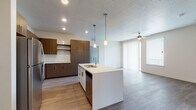 This single-floor residence showcases a contemporary open-concept layout that connects the kitchen, dining, and living areas seamlessly. The kitchen is a standout feature, centered around a large island with a double sink and pendant lighting overhead. Rich, dark wood-tone cabinetry lines the walls alongside white quartz countertops, a white subway tile backsplash, and a full suite of stainless steel appliances including a gas range, over-the-range microwave, dishwasher, and refrigerator. Recessed lighting throughout keeps the space bright and functional.

The living area is finished with wood-style plank flooring and benefits from abundant natural light through a sliding glass door that opens to a private balcony, complemented by a ceiling fan. The bedrooms feature plush neutral-toned carpeting and windows that bring in additional daylight, with one bedroom offering views of the surrounding neighborhood.

Two bathrooms are finished consistently with wood-tone vanities, white quartz countertops, hardwood-style flooring, and tub-shower combinations with built-in shelving. The overall palette of warm neutrals and modern finishes gives the space a clean, cohesive aesthetic throughout.