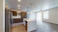 This single-floor residence showcases a contemporary open-concept layout that connects the kitchen, dining, and living areas seamlessly. The kitchen is a standout feature, centered around a large island with a double sink and pendant lighting overhead. Rich, dark wood-tone cabinetry lines the walls alongside white quartz countertops, a white subway tile backsplash, and a full suite of stainless steel appliances including a gas range, over-the-range microwave, dishwasher, and refrigerator. Recessed lighting throughout keeps the space bright and functional.

The living area is finished with wood-style plank flooring and benefits from abundant natural light through a sliding glass door that opens to a private balcony, complemented by a ceiling fan. The bedrooms feature plush neutral-toned carpeting and windows that bring in additional daylight, with one bedroom offering views of the surrounding neighborhood.

Two bathrooms are finished consistently with wood-tone vanities, white quartz countertops, hardwood-style flooring, and tub-shower combinations with built-in shelving. The overall palette of warm neutrals and modern finishes gives the space a clean, cohesive aesthetic throughout.