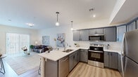 This thoughtfully designed one-bedroom, one-bathroom residence in Mount Wolf, Pennsylvania offers a modern open-concept layout that maximizes every square foot. The combined kitchen and living area serves as the heart of the home, featuring light-toned luxury vinyl plank flooring that flows seamlessly throughout. The kitchen is a standout, outfitted with sleek gray shaker cabinetry, a full suite of stainless steel appliances, and a bright white countertop peninsula with bar seating for three — illuminated by stylish globe pendant lights. The adjacent living room is bathed in natural light from a sliding glass door that opens to the exterior, creating an airy and inviting atmosphere. The spacious primary bedroom offers plush carpeting, a ceiling fan, a large window with outdoor views, and generous closet space. The full bathroom features wood-look flooring, a tub-shower combination, and clean, neutral finishes. A dedicated in-unit laundry closet with a full-size washer and dryer adds everyday convenience. Throughout the space, recessed lighting and a neutral color palette create a clean, contemporary ambiance well-suited for comfortable daily living.