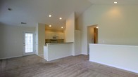 Located at 3900 Suffolk Dr in Dublin, Ohio, this single-floor home offers a thoughtfully designed open-concept layout that maximizes both space and functionality. The living area is highlighted by soaring vaulted ceilings and recessed lighting, creating a bright and airy atmosphere. Plush wall-to-wall carpeting adds warmth and comfort to the main living space, which flows seamlessly toward a natural light source via a glass-paneled entry door.

The kitchen is positioned at the heart of the home and features white raised-panel cabinetry that extends to the ceiling, offering generous storage. A peninsula with a breakfast bar serves as a natural divide between the kitchen and the living area while maintaining the open feel. The kitchen is equipped with a white electric range, an over-the-range microwave, and light-toned countertops, all set on easy-care tile flooring. Recessed lighting throughout keeps the space well-illuminated.

A hallway visible from the main living area leads to additional rooms, providing a clear and logical flow throughout the home. The neutral color palette of warm beige tones across the walls, carpeting, and cabinetry creates a cohesive and inviting atmosphere throughout this Dublin residence.