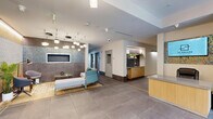 Located at 3459 Butler St in Pittsburgh's Lawrenceville neighborhood, this single-floor amenity space offers a well-appointed fitness and common area experience. The layout includes two hallways and a dedicated exercise room, all designed with a clean, modern aesthetic.

The entry hallway makes an impressive first impression with large-format porcelain tile flooring, a glass vestibule entry with floor-to-ceiling windows that flood the space with natural light, and a warm accent wall featuring light wood paneling paired with textured tile. Contemporary pendant lighting adds a polished finishing touch.

The interior hallway opens into a stylish lounge and reception area, complete with mosaic tile accent walls, pendant lighting clusters, a wall-mounted display screen, and a built-in service counter with warm wood cabinetry. Seating areas with modern furniture invite comfortable gathering.

The spacious exercise room is comprehensively outfitted with cardio equipment including treadmills, an elliptical, a stair climber, and a stationary bike, as well as strength training benches, a multi-rack storage unit holding barbells, kettlebells, and medicine balls, and additional free weights. Large windows bring in natural light and outdoor views, while flush ceiling light panels ensure bright, even illumination throughout. The durable, cushioned flooring is practical and well-suited for a wide range of workouts.
