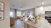 This single-story, one-bedroom, one-bathroom unit is designed with a thoughtful open-concept layout that seamlessly connects the kitchen, dining, and living areas. Wood-style flooring runs throughout, providing a cohesive and contemporary aesthetic across all spaces.

The kitchen is a standout feature, equipped with crisp white shaker cabinetry, stainless steel appliances—including a refrigerator, range, microwave, and dishwasher—and a grey quartz-style countertop. A central island with bar seating and pendant lighting overhead makes it equally functional and stylish. Recessed lighting adds a clean, modern finish.

The living area is generously sized, bathed in natural light from large windows dressed with blinds and decorative curtains. A ceiling fan adds comfort, and neutral warm-toned walls create an inviting atmosphere throughout.

The bedroom is a well-proportioned retreat with ample natural light, a ceiling fan, and windows with blinds. Its warm tones and wood-style flooring carry through cohesively from the rest of the unit.

The bathroom features white cabinetry, a dark countertop, a tiled walk-in shower, and wood-style flooring, reflecting the same clean, modern design language found throughout the space.