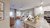 This single-story, one-bedroom, one-bathroom unit is designed with a thoughtful open-concept layout that seamlessly connects the kitchen, dining, and living areas. Wood-style flooring runs throughout, providing a cohesive and contemporary aesthetic across all spaces.

The kitchen is a standout feature, equipped with crisp white shaker cabinetry, stainless steel appliances—including a refrigerator, range, microwave, and dishwasher—and a grey quartz-style countertop. A central island with bar seating and pendant lighting overhead makes it equally functional and stylish. Recessed lighting adds a clean, modern finish.

The living area is generously sized, bathed in natural light from large windows dressed with blinds and decorative curtains. A ceiling fan adds comfort, and neutral warm-toned walls create an inviting atmosphere throughout.

The bedroom is a well-proportioned retreat with ample natural light, a ceiling fan, and windows with blinds. Its warm tones and wood-style flooring carry through cohesively from the rest of the unit.

The bathroom features white cabinetry, a dark countertop, a tiled walk-in shower, and wood-style flooring, reflecting the same clean, modern design language found throughout the space.