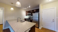 Located at 1600 W Lane Ave in Upper Arlington, Ohio, this single-floor residence offers a well-appointed layout with thoughtful finishes throughout. The open-concept kitchen serves as a central hub, featuring dark espresso cabinetry, stainless steel appliances including a refrigerator, range, and built-in microwave, and a large granite-topped island with an undermount sink and pendant lighting overhead. Track lighting adds a modern touch to the kitchen's overall design. Rich hardwood flooring extends through the main living area, which benefits from a sliding glass door that invites natural light and outdoor views. The bedrooms are finished with plush carpeting and include generous closet space with built-in shelving systems. The primary bathroom is equipped with a dual-sink vanity topped in granite, dark cabinetry, large-format tile flooring, and a glass-enclosed walk-in shower. A second full bathroom mirrors the same design aesthetic with granite countertops, dark cabinetry, and a full tub-shower combination. Neutral warm tones on the walls and consistent high-quality finishes throughout lend the space a cohesive, polished ambiance suited for comfortable everyday living.
