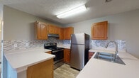 Located at 2800 John Steven Way in Reynoldsburg, Ohio, this single-floor unit offers a well-organized and functional layout designed for comfortable everyday living. The kitchen is a standout feature, outfitted with warm honey-toned cabinetry, stainless steel appliances including a refrigerator and electric range, a mosaic tile backsplash, and light countertops that extend into a peninsula-style breakfast bar. This peninsula creates a seamless visual connection to the adjacent living area, which transitions from wood-look flooring into plush carpeting. The living space is open and bright, benefiting from natural light and a neutral color palette of soft grays and warm whites throughout. The bedrooms are carpeted and feature large windows that invite natural light, along with generously sized closets equipped with built-in shelving and hanging rods. The bathroom includes a wide vanity with a light countertop, a large mirror with overhead lighting, and additional built-in shelving for storage. Textured ceilings are present throughout the unit. The overall ambiance is clean, neutral, and move-in ready, offering a practical and comfortable living environment in the Reynoldsburg community.