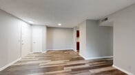 This single-floor residence offers a practical and comfortable layout designed for everyday living. The open living and dining area is finished with durable wood-look plank flooring in warm, neutral tones, complemented by light gray walls and a textured ceiling. A sliding glass door fills the space with natural light and provides access to an outdoor area with surrounding greenery. The kitchen is efficiently arranged in a galley-style configuration, featuring rich dark wood cabinetry, granite-style countertops, a stainless steel double sink, and black appliances including an electric range with overhead ventilation and a full-size refrigerator. A dedicated utility door is accessible directly from the kitchen. The bedroom is a calm, private retreat finished with soft wall-to-wall carpeting and a window with blinds that frame outdoor views. The bathroom is well-appointed with a granite-topped vanity, dark wood cabinetry, a large wall mirror with integrated lighting, and a full tub-shower combination with chrome fixtures. Throughout the residence, white baseboards and clean wall finishes contribute to a cohesive, move-in-ready aesthetic.