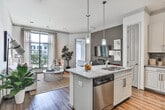 Located at 2370 Main St NW in Duluth, GA, this well-designed single-floor residence offers a thoughtfully laid-out living experience with modern finishes throughout. The open-concept kitchen serves as a central hub, showcasing granite countertop surfaces, a large center island with seating, white shaker-style cabinetry, a stone tile backsplash, stainless steel appliances, and a dedicated pantry for ample storage. Pendant lighting and track lighting illuminate the space, which flows seamlessly onto rich hardwood flooring extending into the living and dining areas. The living room is bright and welcoming, featuring large floor-to-ceiling windows that invite abundant natural light and offer views of the surrounding outdoor amenities. Crown molding adds a refined architectural touch throughout. The bedrooms are carpeted and generously sized, each featuring large windows with sheer drapery that frame outdoor courtyard views, creating a calm and airy retreat. The bathroom is well-appointed with a wraparound dual-sink vanity, granite countertops, white cabinetry with brushed nickel hardware, and a large mirror with overhead lighting. Overall, the space presents a cohesive, contemporary aesthetic with upscale finishes and a comfortable, functional layout.