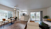 This single-floor residence offers a thoughtfully designed open-concept layout that seamlessly connects the kitchen, dining, and living areas. The kitchen features crisp white shaker cabinetry, light quartz countertops, stainless steel appliances including a refrigerator, range, microwave, and dishwasher, and wood-look flooring that extends throughout the main living space. A peninsula counter provides additional prep space and a natural division between the kitchen and living area. The living room is highlighted by a classic corner fireplace with a white surround, built-in shelving, and large sliding glass doors that open to a private balcony, filling the space with natural light and outdoor views. The spacious primary bedroom is finished with plush carpeting, vaulted ceilings, and a generous window with outdoor views. It connects directly to a dedicated vanity area and a walk-in closet. Two full bathrooms serve the unit: one with a tiled tub-shower combination accented by contrasting tile details and a privacy window, and a second featuring a walk-in shower with a glass door, white vanity with quartz countertop, and wood-look flooring. A hallway connects all areas efficiently, with two closets offering ample storage throughout the residence.