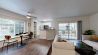 This single-floor residence offers a thoughtfully designed open-concept layout that seamlessly connects the kitchen, dining, and living areas. The kitchen features crisp white shaker cabinetry, light quartz countertops, stainless steel appliances including a refrigerator, range, microwave, and dishwasher, and wood-look flooring that extends throughout the main living space. A peninsula counter provides additional prep space and a natural division between the kitchen and living area. The living room is highlighted by a classic corner fireplace with a white surround, built-in shelving, and large sliding glass doors that open to a private balcony, filling the space with natural light and outdoor views. The spacious primary bedroom is finished with plush carpeting, vaulted ceilings, and a generous window with outdoor views. It connects directly to a dedicated vanity area and a walk-in closet. Two full bathrooms serve the unit: one with a tiled tub-shower combination accented by contrasting tile details and a privacy window, and a second featuring a walk-in shower with a glass door, white vanity with quartz countertop, and wood-look flooring. A hallway connects all areas efficiently, with two closets offering ample storage throughout the residence.