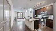 Located at Talavera Ridge in San Antonio, TX, this well-appointed 2-bedroom, 2-bathroom residence offers a thoughtfully designed single-level layout. The open-concept living and kitchen area serves as the heart of the home, showcasing rich dark wood cabinetry, a granite-topped island with a built-in sink, stainless steel appliances, and a tasteful tile backsplash. Track and pendant lighting illuminate the space, while durable hardwood-style flooring flows throughout the main living areas. The living room is bright and airy, with a ceiling fan and French doors that invite natural light and provide outdoor access. Both bedrooms feature plush carpeting, ceiling fans, and generous natural light from large windows. The primary bedroom connects directly to its en-suite bathroom, which is finished with granite countertops, dark wood cabinetry, dual sinks, and classic tile flooring. Each bedroom is served by a spacious walk-in closet outfitted with multi-level shelving and hanging rods, offering abundant storage. A hallway connects the rooms, adding to the functional flow of the layout. The overall ambiance is modern and clean, with a neutral color palette that complements the upscale finishes throughout.