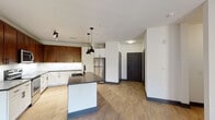 This single-floor residence showcases a thoughtfully designed open-concept layout that seamlessly connects the kitchen and living areas. The kitchen is a standout feature, combining rich dark-stained upper cabinetry with crisp white lower cabinets, all accented by sleek black hardware. A marble-style tile backsplash adds texture, while dark quartz countertops extend across both the perimeter surfaces and the central island, which is equipped with an undermount sink. Stainless steel appliances, including a refrigerator, range, and microwave, complete the culinary space. Pendant lighting over the island and track lighting overhead enhance the kitchen's modern aesthetic. Light wood-look flooring flows through the kitchen and living area, which features a ceiling fan and French doors that invite natural light and outdoor access. The bedrooms are finished with plush carpeting, bold dark baseboards, and ceiling fans, offering a comfortable retreat. The primary bathroom impresses with an expansive dual-sink vanity topped with warm quartz counters, a backlit mirror, large-format tile flooring, a soaking tub, and a glass-enclosed shower with subway tile surround. Dark door frames and hardware provide a consistent, contemporary design thread throughout the entire space.