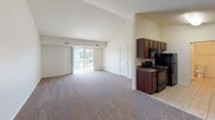 Located at 489 Tyler Ln in Grand Haven, Michigan, this single-floor unit offers a practical and well-organized layout designed for comfortable everyday living. The open-concept living area is generously sized, featuring neutral-toned carpet and vaulted ceilings that lend a sense of openness and volume to the space. A large sliding glass door floods the living area with natural light and provides direct outdoor access, enhancing the bright, airy atmosphere throughout.

The galley-style kitchen is efficiently arranged with rich, dark wood cabinetry lining both walls, dark granite-style countertops, tile flooring, and black appliances including a range and refrigerator. A doorway from the kitchen connects directly to a full bathroom, adding convenience to the floor plan.

The bedrooms continue the neutral carpeted aesthetic, with tall walls and multiple doorways offering practical access to closets and adjoining spaces. The bathroom features a clean, white tub and shower combination with chrome fixtures and tile flooring.

A dedicated in-unit laundry closet houses a full-size washer and dryer, providing added functionality. The overall design emphasizes clean lines, neutral finishes, and efficient use of space throughout the home.