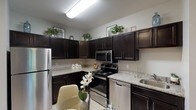 This single-floor residence offers a thoughtfully designed layout that balances functionality and comfort across its key living spaces. The kitchen is a standout feature, showcasing rich dark cabinetry that extends to the upper walls, light granite countertops, and a full suite of stainless steel appliances including a refrigerator, range, microwave, and dishwasher. Light wood-style flooring runs throughout, complementing the neutral color palette. Conveniently adjacent to the kitchen is a dedicated laundry nook with a stacked washer and dryer unit, along with space for a dining table. The living room receives generous natural light through a large window framing lush outdoor greenery. A ductless mini-split system provides climate control, and the space is finished with light hardwood flooring and warm, neutral wall tones. Both bedrooms are well-sized and serene, each featuring windows with outdoor views, light flooring, and ample closet space — one bedroom includes a walk-in closet. The full bathroom is finished with large-format tile flooring and includes a shower-tub combination. Throughout, the residence maintains a cohesive, neutral aesthetic that feels both practical and inviting.