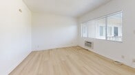 Located at 1011 E Palmer Ave in Glendale, California, this single-floor 2-bedroom, 1-bathroom unit offers a clean, minimalist aesthetic defined by crisp white walls and light wood-style flooring that runs consistently throughout every room.

The combined kitchen and living area forms the heart of the unit. The kitchen is equipped with white cabinetry, a stainless steel refrigerator, and a countertop range. A ceiling fan with a matte black finish adds a modern touch to this shared space, providing both style and comfort.

Both bedrooms are bright and well-proportioned, featuring large windows fitted with horizontal blinds that allow for generous natural light and views of the surrounding Glendale neighborhood. The primary bedroom includes a built-in sliding closet, offering practical storage. A wall-mounted HVAC unit is present in one of the bedrooms, providing individual climate control.

The bathroom maintains the same clean aesthetic, with light wood flooring, white walls, a bathtub, a bidet-equipped toilet, and a window that brings in natural light and ventilation.

A hallway connects the main living spaces, contributing to a logical and functional layout. Throughout the unit, textured ceilings and clean white baseboards complement the overall bright and airy atmosphere.