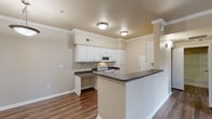 This thoughtfully designed one-bedroom, two-bathroom residence offers a comfortable and functional single-floor layout. The open-concept kitchen and living area serves as the heart of the home, featuring white cabinetry with dark granite-style countertops, white appliances including a refrigerator, electric range, and built-in microwave, along with a peninsula that provides additional prep and seating space. Crown molding accents the ceilings throughout, adding a refined architectural touch.

The living room is bright and inviting, with dark hardwood-style flooring, a white-mantled fireplace, and sliding glass doors that open to a private balcony with outdoor views. The bedroom is carpeted for comfort and includes a mirrored sliding-door closet with built-in shelving, as well as a ceiling fan overhead.

Both bathrooms are finished with warm neutral tones, white vanity cabinetry, and wood-style flooring. An additional walk-in closet is accessible from the hallway, providing generous storage. The unit is completed by a dedicated hallway connecting each space efficiently. Warm beige walls and consistent finishes throughout create a cohesive and welcoming ambiance.