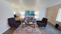 Located at 9900 Spain Rd NE in Albuquerque, New Mexico, this single-floor residence offers a cohesive mid-century modern aesthetic carried throughout each room. The living area serves as the centerpiece of the home, featuring wood-look flooring, a textured ceiling, and generous natural light filtered through vertical blinds. The space is open and inviting, with room for a full seating arrangement anchored by a plush area rug and glass coffee table.

The galley-style kitchen is efficiently designed with warm wood cabinetry, dark granite-style countertops, and black appliances including a range and refrigerator. It opens directly into a dedicated dining area distinguished by a bold terracotta accent wall, pendant lighting, and a glass-top dining table — creating a vibrant and intimate setting for meals.

A cozy breakfast nook with a matching terracotta accent wall and natural light provides an additional casual dining option. The bedroom is bright and comfortable, featuring plush carpet, mirrored sliding closet doors, a window that brings in ample sunlight, and a warm orange accent wall that adds personality and depth.

The bathroom includes a long vanity with wood cabinetry and dark countertops, a large mirror, and a separate tub-shower combination with white tile surround, offering practical functionality throughout.