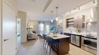 Located at 100 King Rail Dr, Unit 103 in Lynnfield, MA, this thoughtfully designed one-bedroom, one-bathroom residence offers a cohesive open-concept layout that maximizes every square foot. The kitchen serves as a centerpiece, featuring two-tone cabinetry with rich dark lower cabinets and lighter upper storage, quartz countertops, a subway tile backsplash, stainless steel appliances including a range with a wall-mounted hood, and a dishwasher. A central island with pendant lighting provides seating for casual dining. The kitchen flows seamlessly into the living room, which is finished with plush carpeting, neutral tones, and large windows that allow ample natural light and outdoor views. The bedroom is a calm retreat, offering corner windows with serene green landscape views, soft carpeting, and a well-proportioned layout with closet access. The bathroom is clean and functional, featuring a tub-shower combination, a vanity with storage, and tile flooring. Throughout the residence, the design palette is cohesive and contemporary, with warm neutrals, track lighting, and modern finishes that create an inviting and practical living environment.