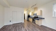 Located at 4744 12th Avenue Northeast in Seattle's vibrant University District, this studio apartment offers a thoughtfully designed open-concept layout that seamlessly integrates the living, dining, and kitchen areas into one cohesive space. The kitchen is well-appointed with stainless steel appliances — including a refrigerator, electric range, microwave, and dishwasher — complemented by light wood cabinetry, dark countertops, and a double sink. Track lighting runs throughout, providing targeted, adjustable illumination across the entire unit. Durable hardwood-style flooring extends continuously through the space, adding warmth and visual continuity. The living area receives natural light through a large sliding glass door that opens onto a private balcony, which overlooks a shared courtyard featuring raised garden beds — a welcoming outdoor amenity. Three closets provide generous storage for a compact unit, helping to maximize organization and functionality. A full bathroom completes the layout. The building's modern exterior and community outdoor spaces reflect a contemporary residential design suited to urban living. This unit is ideally situated for those seeking proximity to the University of Washington, local transit, and the many dining and retail options that define this dynamic Seattle neighborhood.