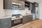 This thoughtfully designed one-bedroom, one-bathroom unit offers a contemporary living experience across a single floor. Light wood-toned flooring flows consistently throughout, creating a cohesive and airy aesthetic. Large floor-to-ceiling sliding glass doors are a defining architectural feature, appearing in both the living room and bedroom, flooding the space with natural light and providing outdoor views of a resort-style pool area and surrounding buildings.

The open-plan living and kitchen area is well-proportioned, with a ceiling fan adding functionality to the bright, white-walled space. The kitchen is outfitted with dark wood cabinetry, granite-style countertops, a white subway tile backsplash, and a full suite of stainless steel appliances including a gas range, over-the-range microwave, dishwasher, and side-by-side refrigerator with ice and water dispenser.

The bedroom is a comfortable size, featuring its own sliding glass door access and views of the outdoor amenity area, along with dedicated closet storage.

The bathroom is finished to a high standard, featuring large-format tile flooring, a dark wood vanity with a white countertop, a wide mirror, and a spacious glass-enclosed walk-in shower with marble-style tile surround, delivering a clean and modern aesthetic.